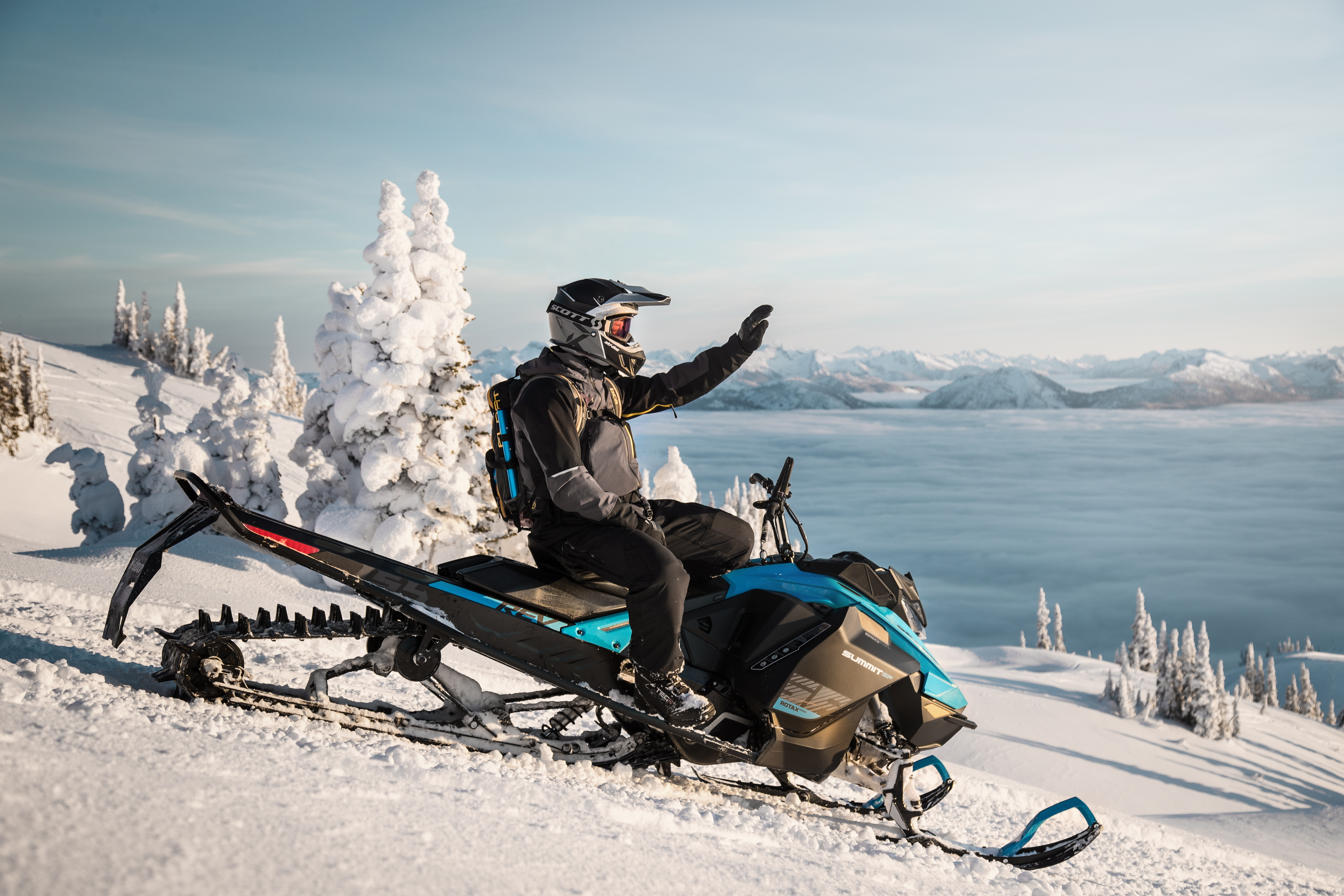 Person waving while sitting on a ski-doo snowmobile using mountain snow tracks
