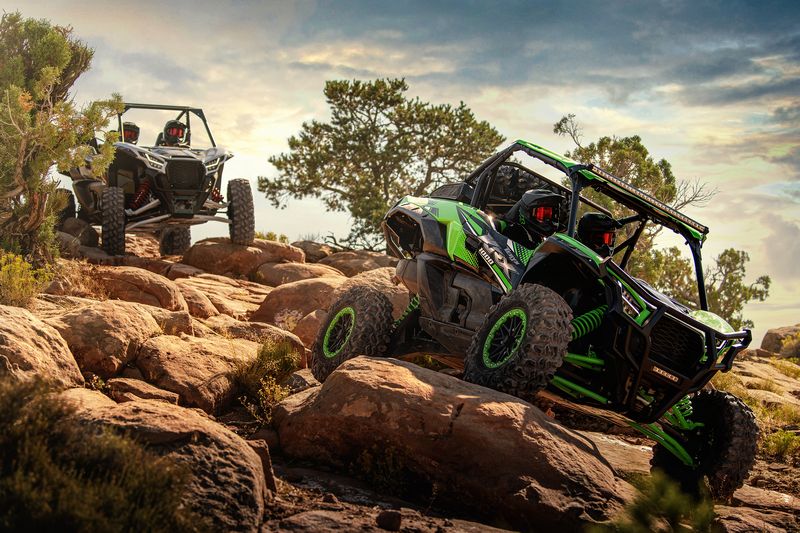 Two SxS take it real slow down a hill with large rocky outcrops that they are driving over.