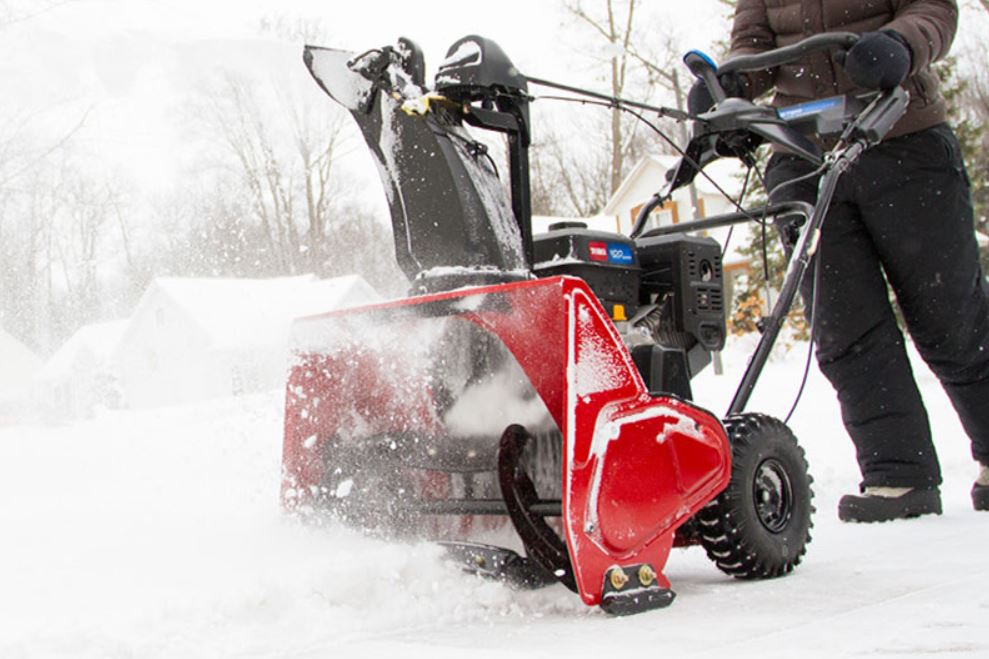 A close up of a person using a toro snowblower to remove snow from their land.