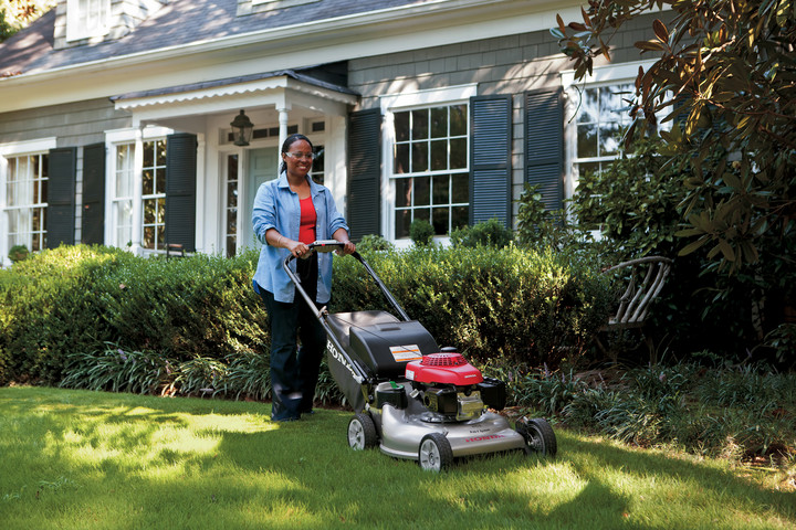 A woman smiles as she pushes her Honda walk behind mower across her manicured front lawn