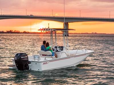 A couple on a Boston Whaler Montauk® 190 boat enjoys the sunset on the water near a bridge.