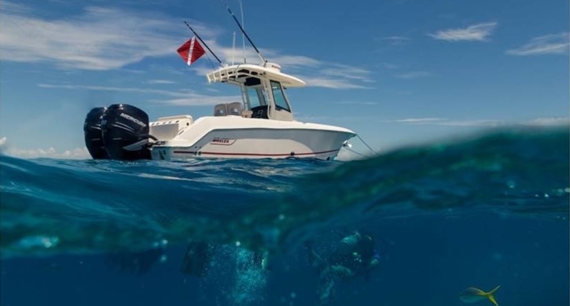 A view of a white Boston Whaler Outrage® from half underwater and half above water with someone scuba diving next to the boat