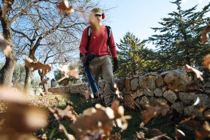 Man blowing away fallen leaves from a stone fence with an ECHO backpack blower