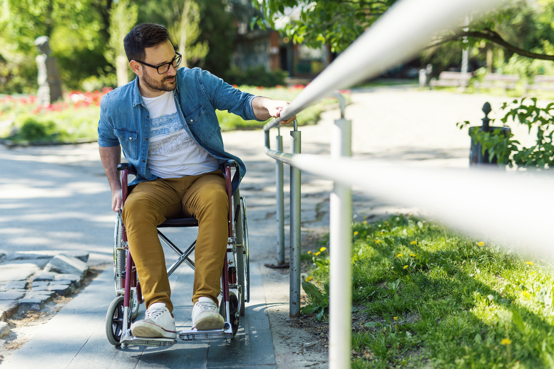 man in a wheelchair, holding on to a hand rail as he goes up a ramp.