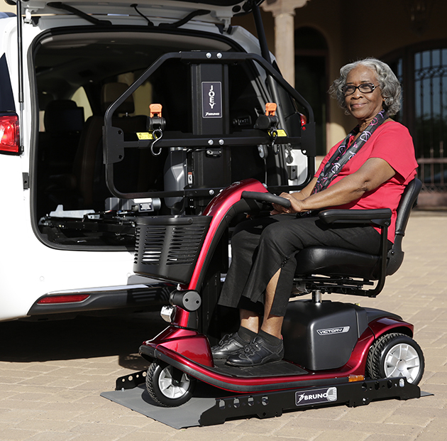 A woman sitting in a mobility scooter on a lift connected to her minivan