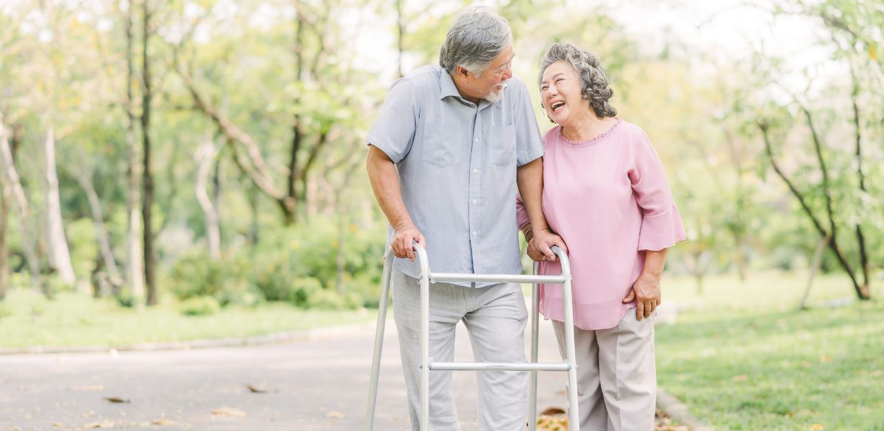 Elderly Couple laughing in a scenic park while man uses walker