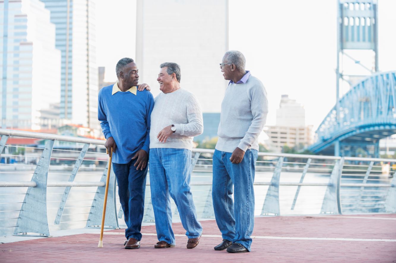 Three senior men walking along with city waterfront with a cane
