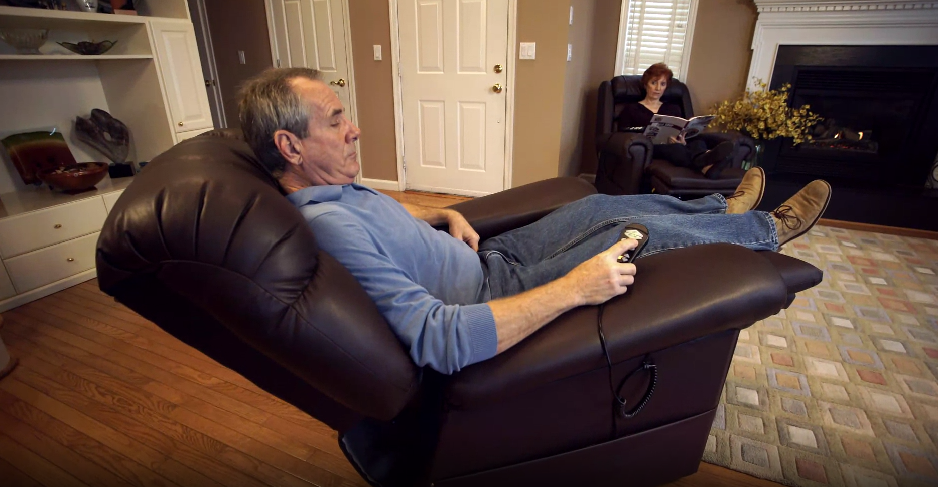 A man sits in his lift chair with the controller in his hand while his wife sits across from him in a chair
