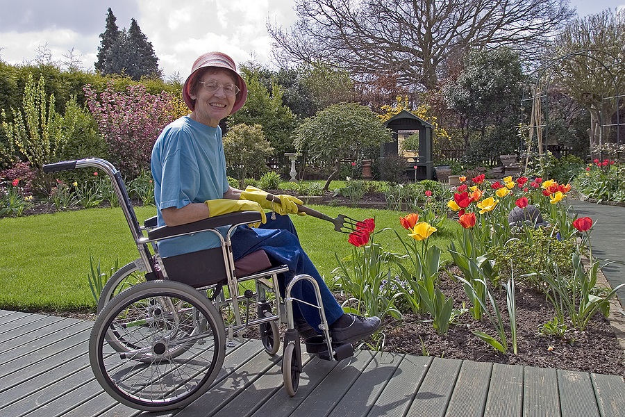 A woman using a wheelchair smiles and poses with her spring garden in full bloom