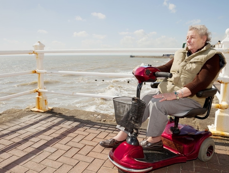 Elderly woman on a mobility scooter looks out over the ocean from a boardwalk
