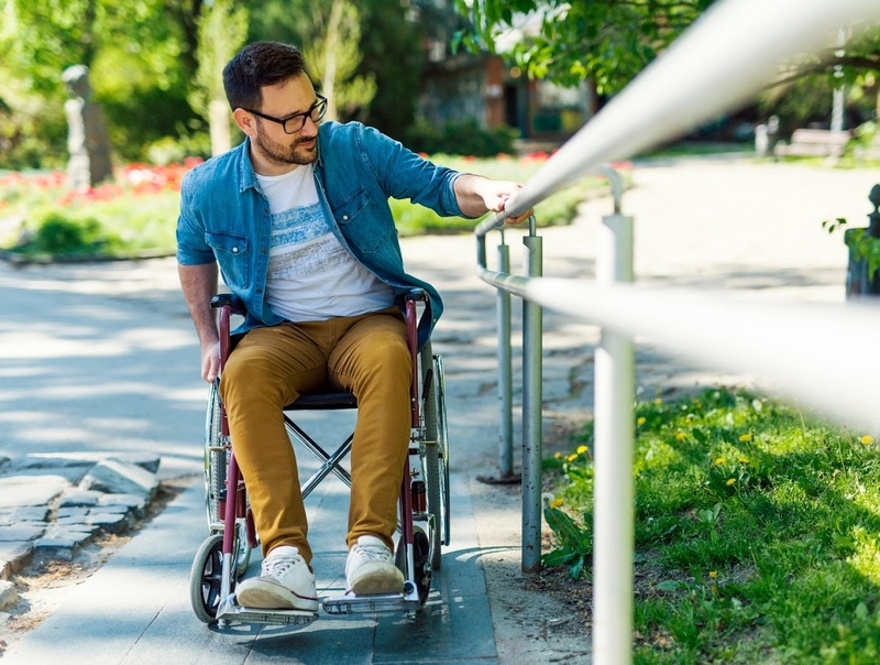Young man on a manual wheelchair pulls himself up a ramp in a courtyard